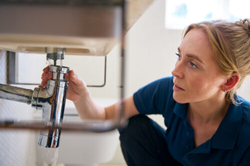 a woman fits a pipe underneath a sink with professional plumbing services